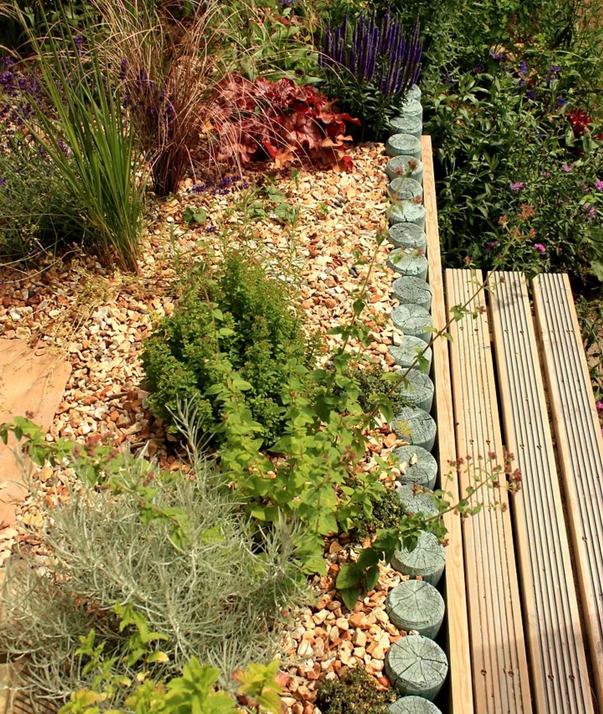 Plants lie in a gravel flowerbed next to a patio